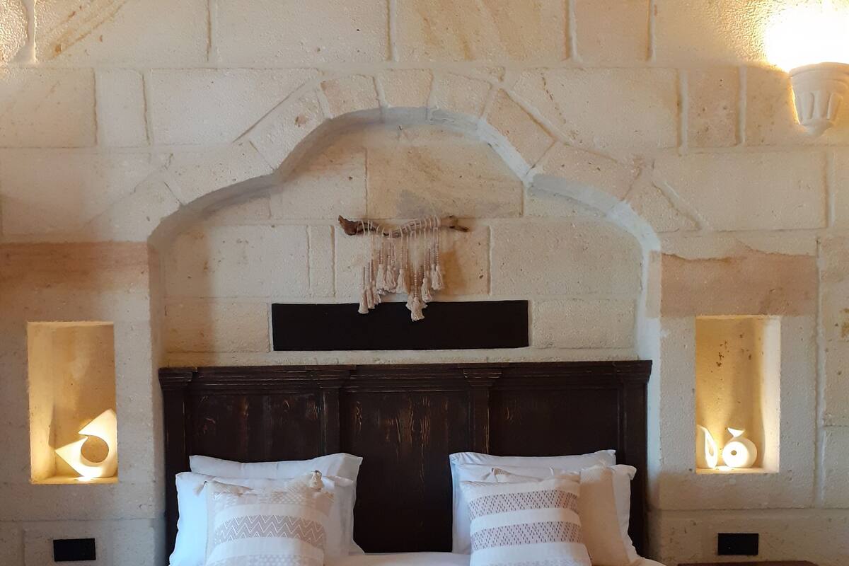 A bedroom with a stone archway, a bed with white bedding, and two wall-mounted lamps.