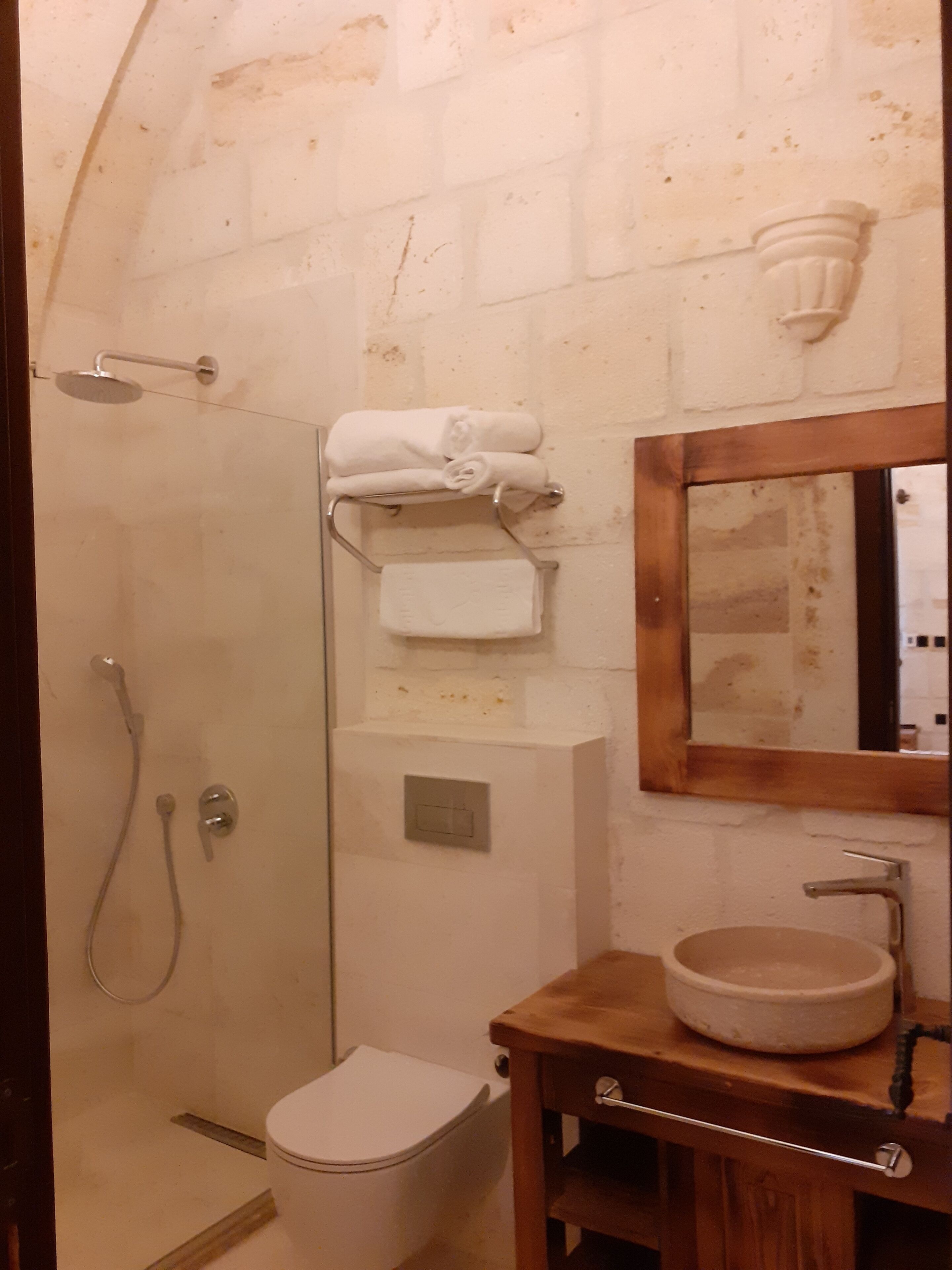 A bathroom with a glass-enclosed shower, a toilet, a wooden vanity with a sink, and a mirror.