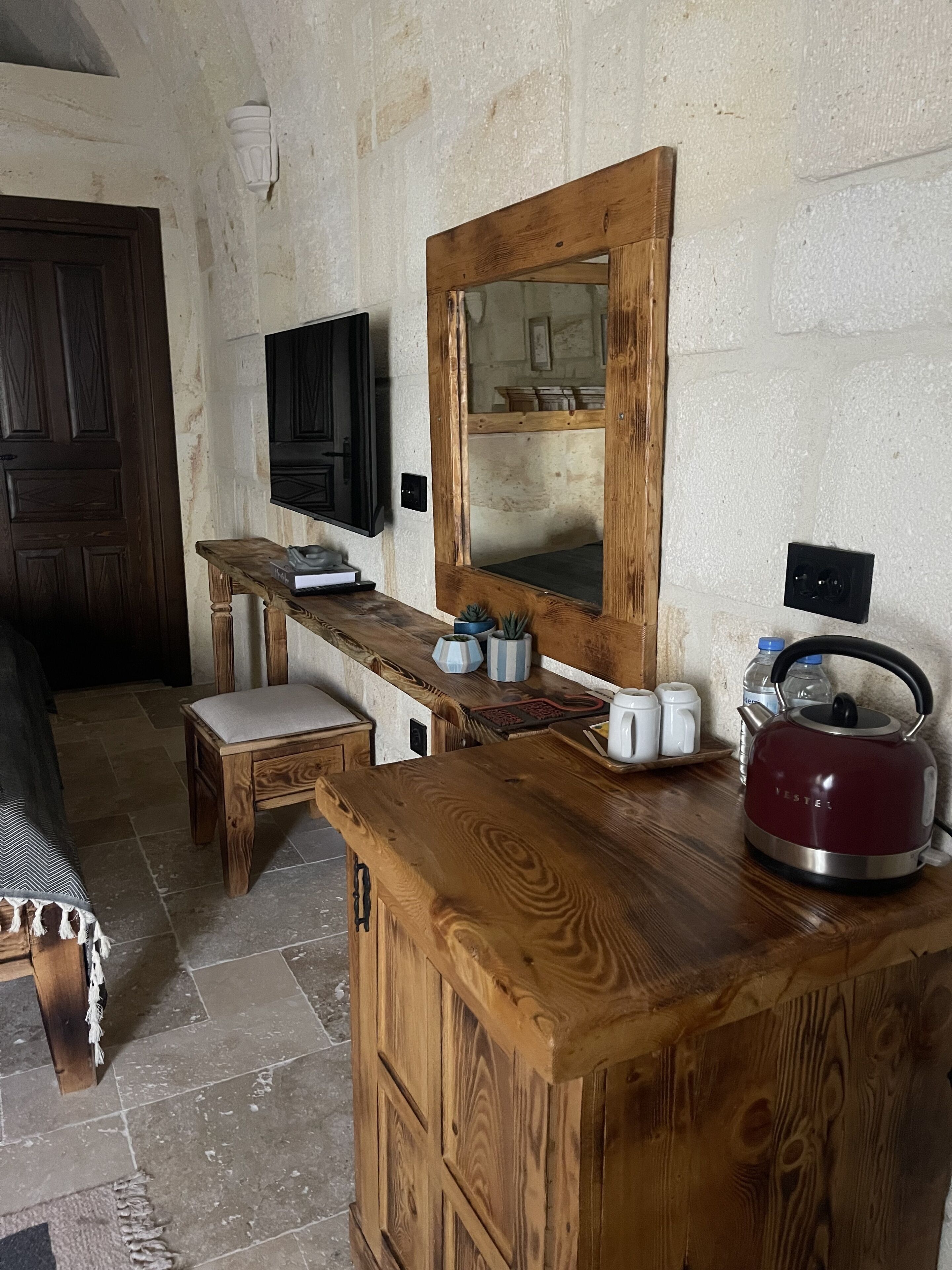 A rustic kitchen with a wooden counter, a kettle, and a mirror.