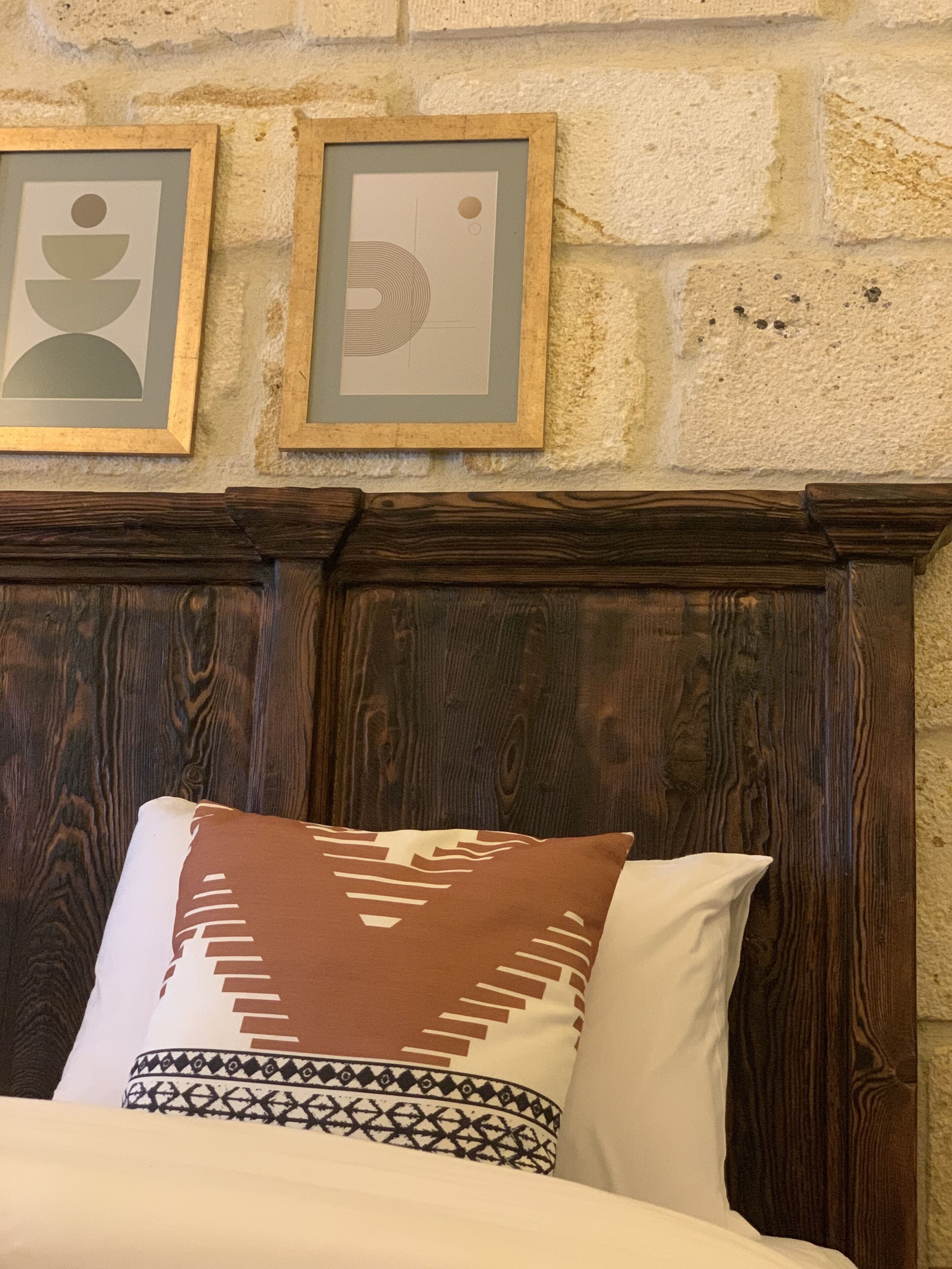 A bed with a patterned pillow and a plain pillow, a wooden headboard, and two framed pictures on the wall.