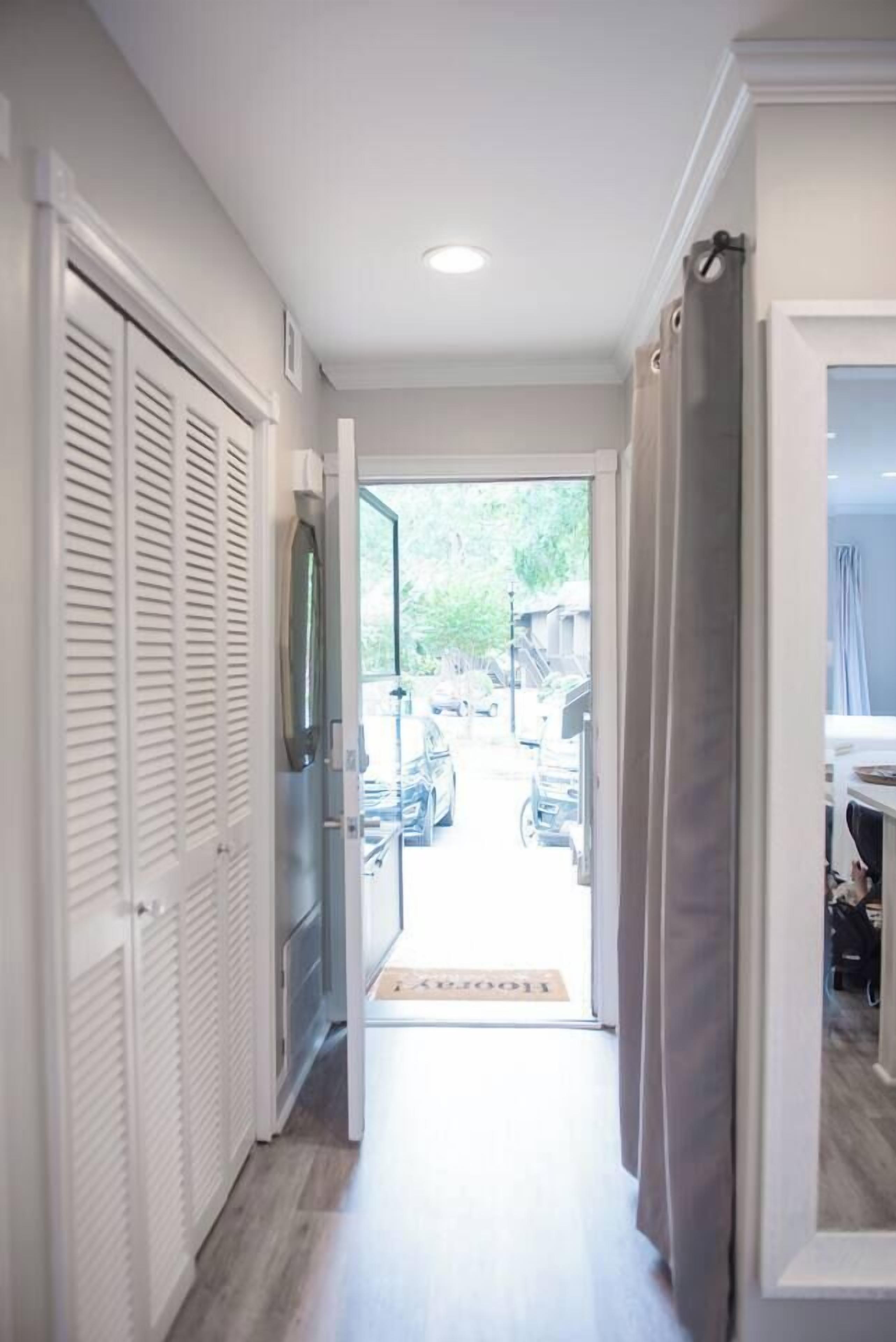 A hallway leading to a door with a view of parked cars outside.