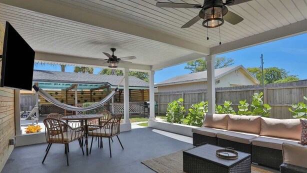 A covered patio with outdoor furniture, a hammock, and a TV mounted on the wall.