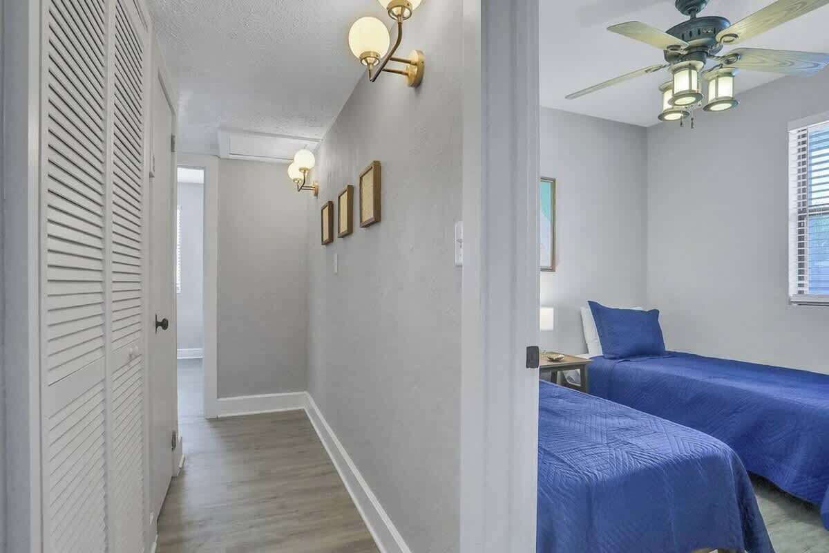 Habitación de hotel con dos camas, ventilador de techo, apliques de pared y ventana con persianas.