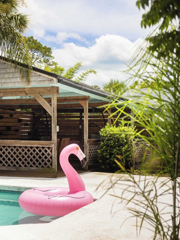 A wooden structure with a glass roof, a pink flamingo float, and a pool.