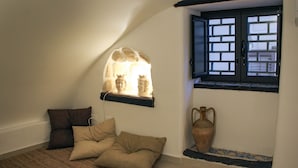 A room with a sloped ceiling, a window with a black frame, a wall-mounted shelf with bust sculptures, a brown sofa, and a vase on the floor. - Cozy apartment in the heart of the historic center of Palermo (Palermo)