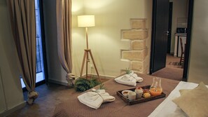 Una habitación de hotel con una cama, una mesita de noche con una bandeja de desayuno, una lámpara y vistas al pasillo.