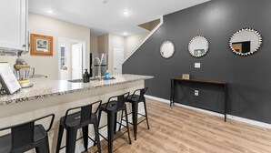 Una cucina con piano di lavoro in granito, sgabelli da bar neri e una parete decorata in grigio scuro con tre specchi ornamentali.