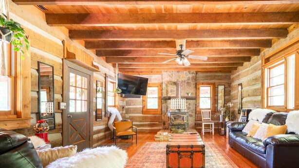 A log cabin interior with a fireplace, leather furniture, and a television. - Stunning Boho Log Cabin Country Retreat with Pool
 (Portland)