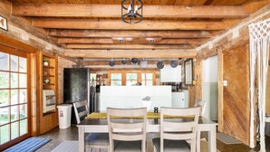 A rustic kitchen with wooden beams, a dining table with chairs, and a view to the outside. - Stunning Boho Log Cabin Country Retreat with Pool
 (Portland)