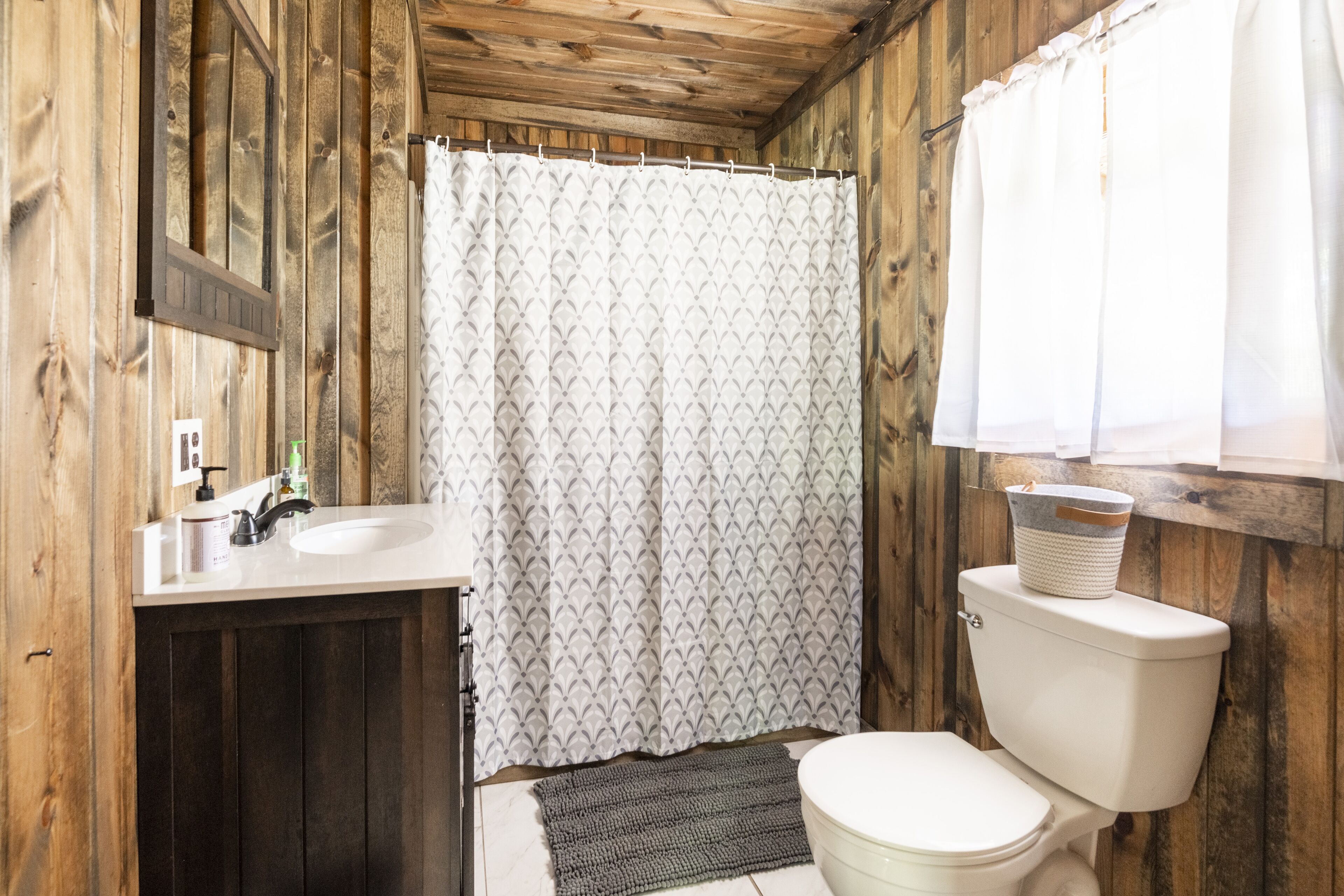 A bathroom with a wooden interior, a white toilet, a sink with a mirror, and a patterned shower curtain.