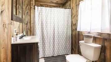 A bathroom with a wooden interior, a white toilet, a sink with a mirror, and a patterned shower curtain.