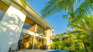 Un moderno edificio de dos pisos con piscina, mobiliario exterior y abundante vegetación.