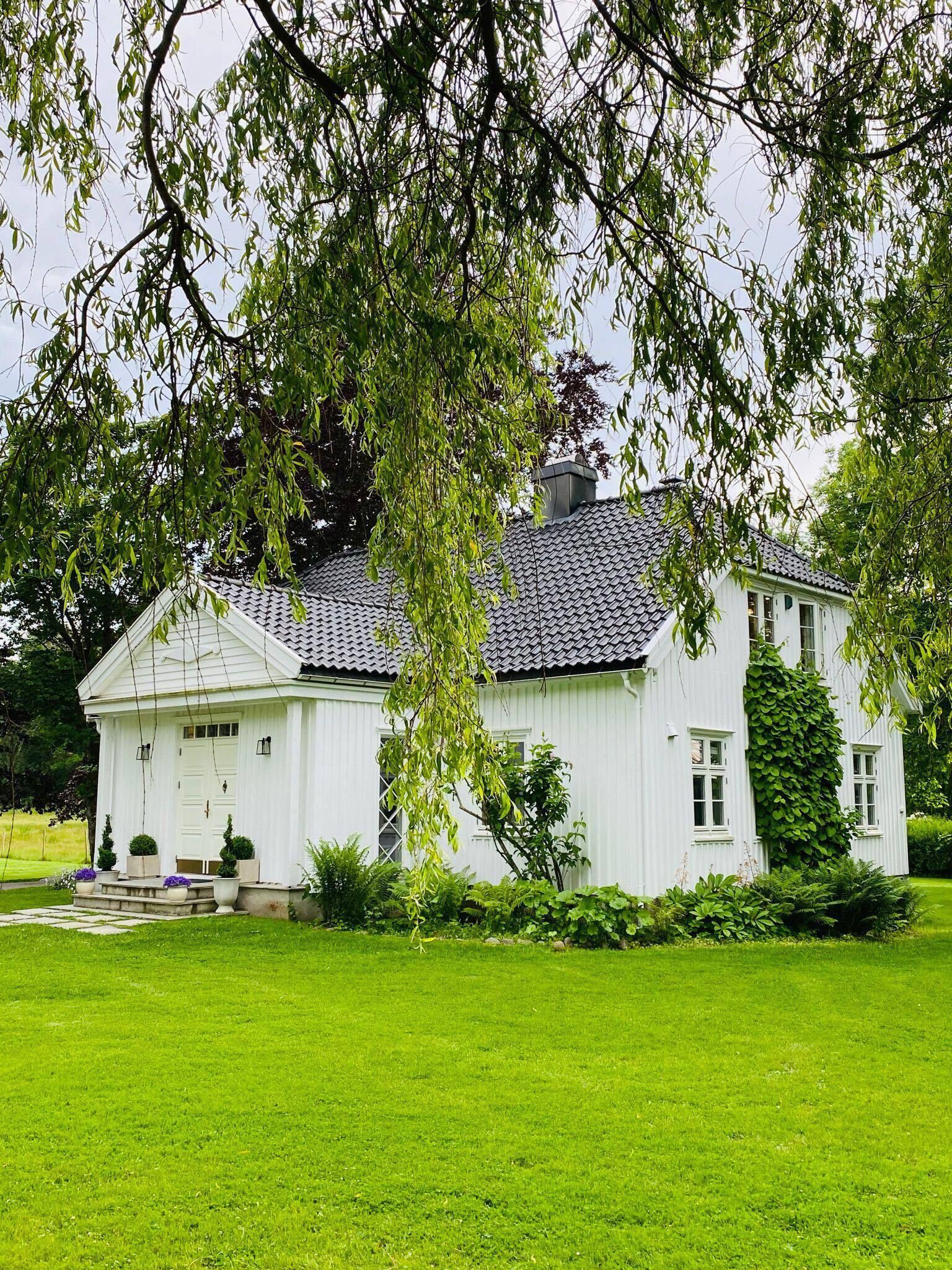 Et hvidt hus med et flisegulv på taget, omgivet af en velplejet græsplæne og træer.