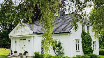 Et hvidt hus med et flisegulv på taget, omgivet af en velplejet græsplæne og træer.