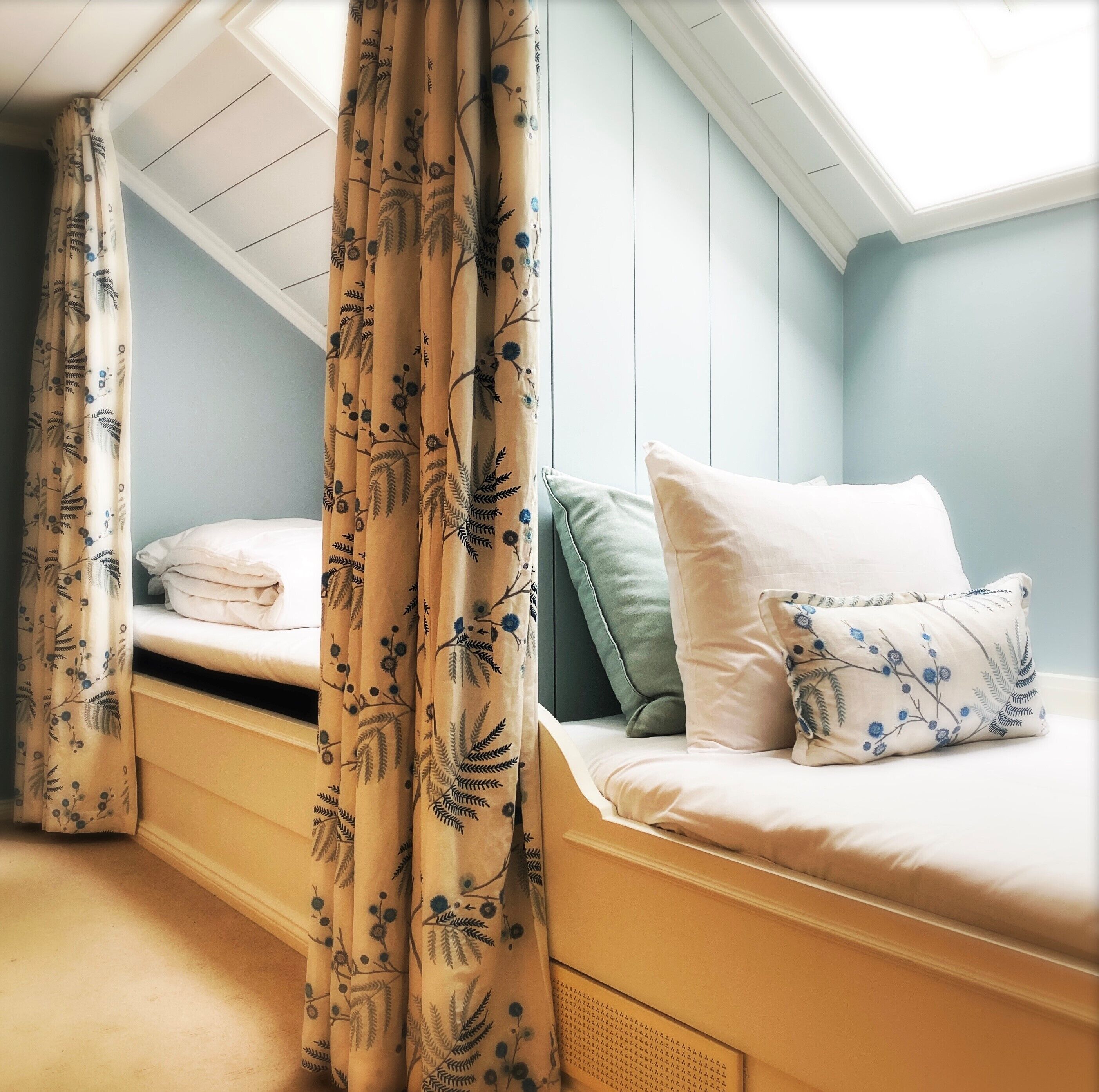 A bedroom with two beds, a skylight, and a window with curtains.