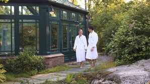A conservatory with a green exterior and large windows, surrounded by lush greenery and a stone pathway. - Engø Gård (Færder)