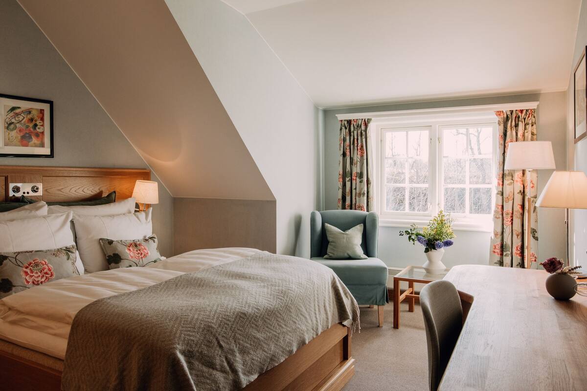A bedroom with a bed, a chair, a table, and a window with curtains.