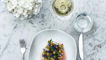 Une assiette blanche contenant un plat, une fourchette, un couteau, un verre de vin blanc et un petit verre d’eau, le tout posé sur une surface en marbre.