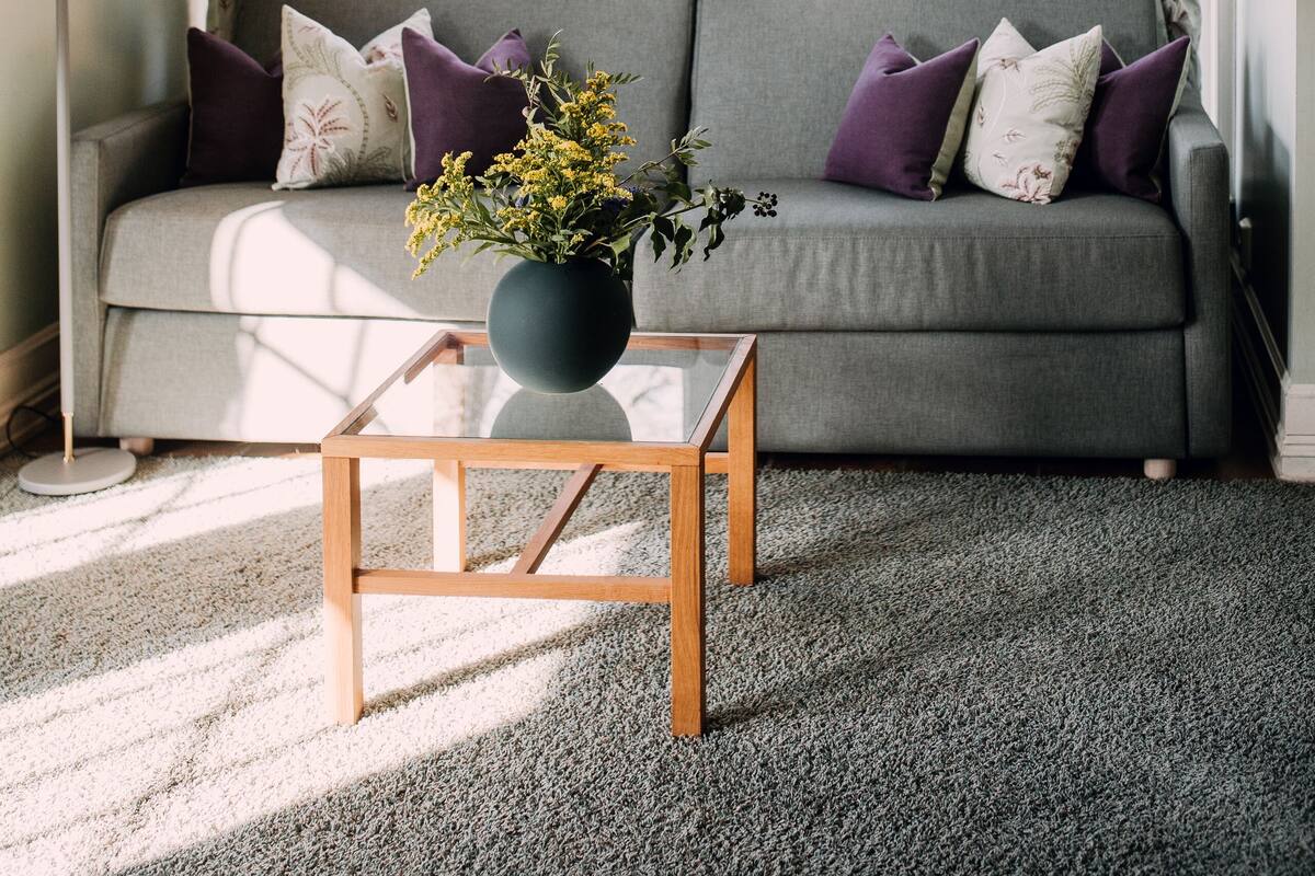 A cozy living room with a grey sofa, purple cushions, a wooden coffee table, and a vase of flowers.