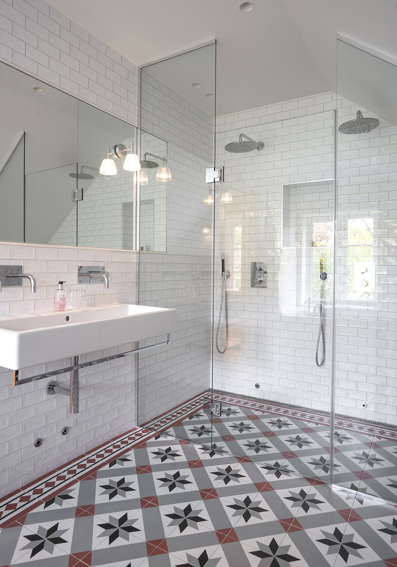 Un baño moderno con ducha envuelta en vidrio, un lavabo blanco con espejo y baldosas de suelo con diseño.