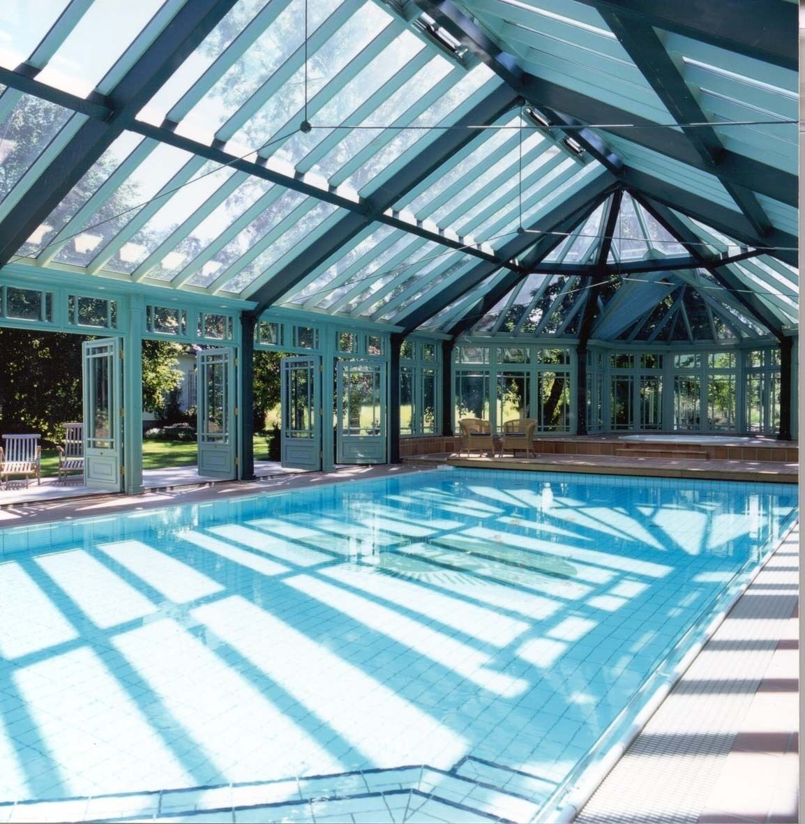 A covered swimming pool with glass panels and a roof structure.