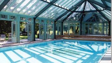 A covered swimming pool with glass panels and a roof structure.