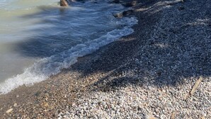 A pebbled beach with clear blue water and a rocky shoreline. - The charming Glenn Cottage! Walk to Lake Michigan! (Fennville)
