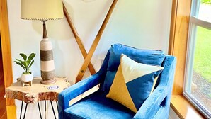 A cozy room with a blue armchair, a wooden paddle wall decoration, a life preserver, a lamp, and a small plant. - The charming Glenn Cottage! Walk to Lake Michigan! (Fennville)