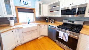 A modern kitchen with white cabinets, a stainless steel stove, and a dishwasher. - The charming Glenn Cottage! Walk to Lake Michigan! (Fennville)