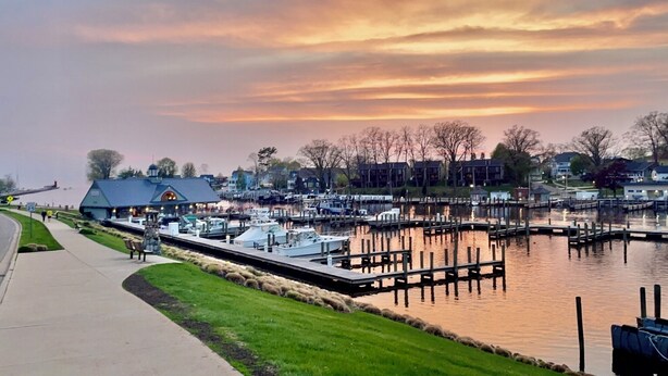 A marina with docked boats, a small building with a blue roof, and a pedestrian pathway alongside the water. - The charming Glenn Cottage! Walk to Lake Michigan! (Fennville)