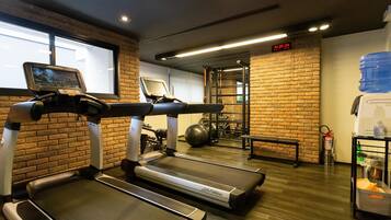 Un gimnasio con cintas de correr, una pantalla digital, una pared de ladrillo, un dispensador de agua y un espejo.