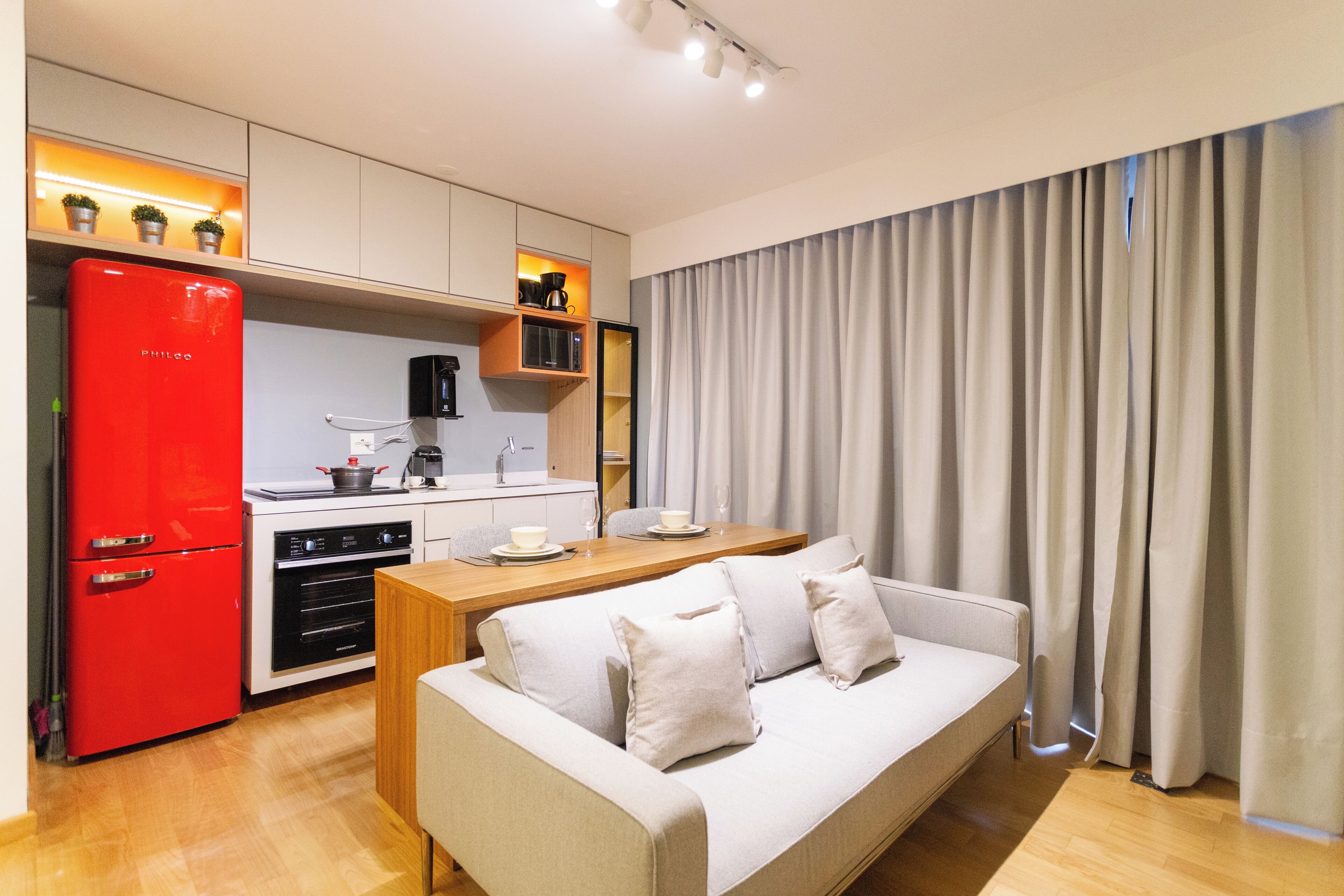 Een moderne keuken met een rode koelkast, een houten eettafel en een beige bank.