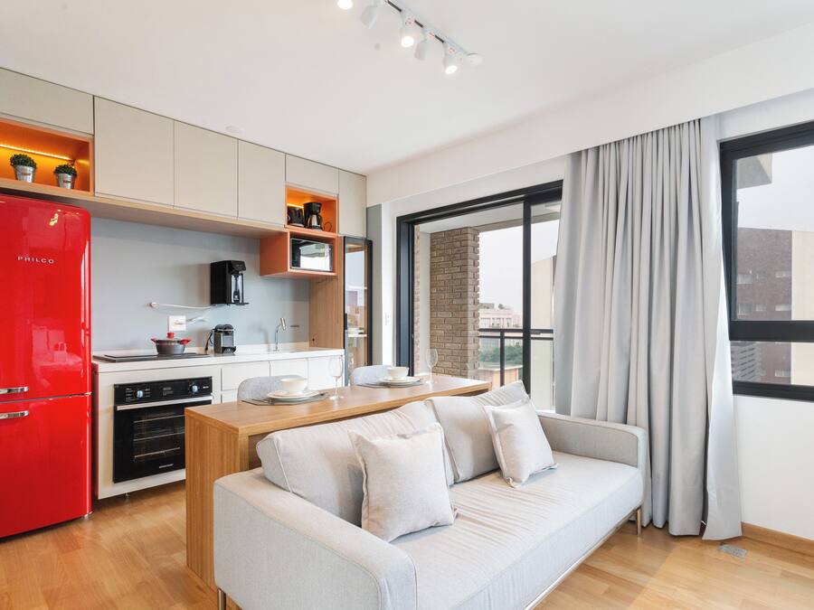 Una cocina moderna con un refrigerador rojo, armarios de madera y un rincón comedor con sofá.