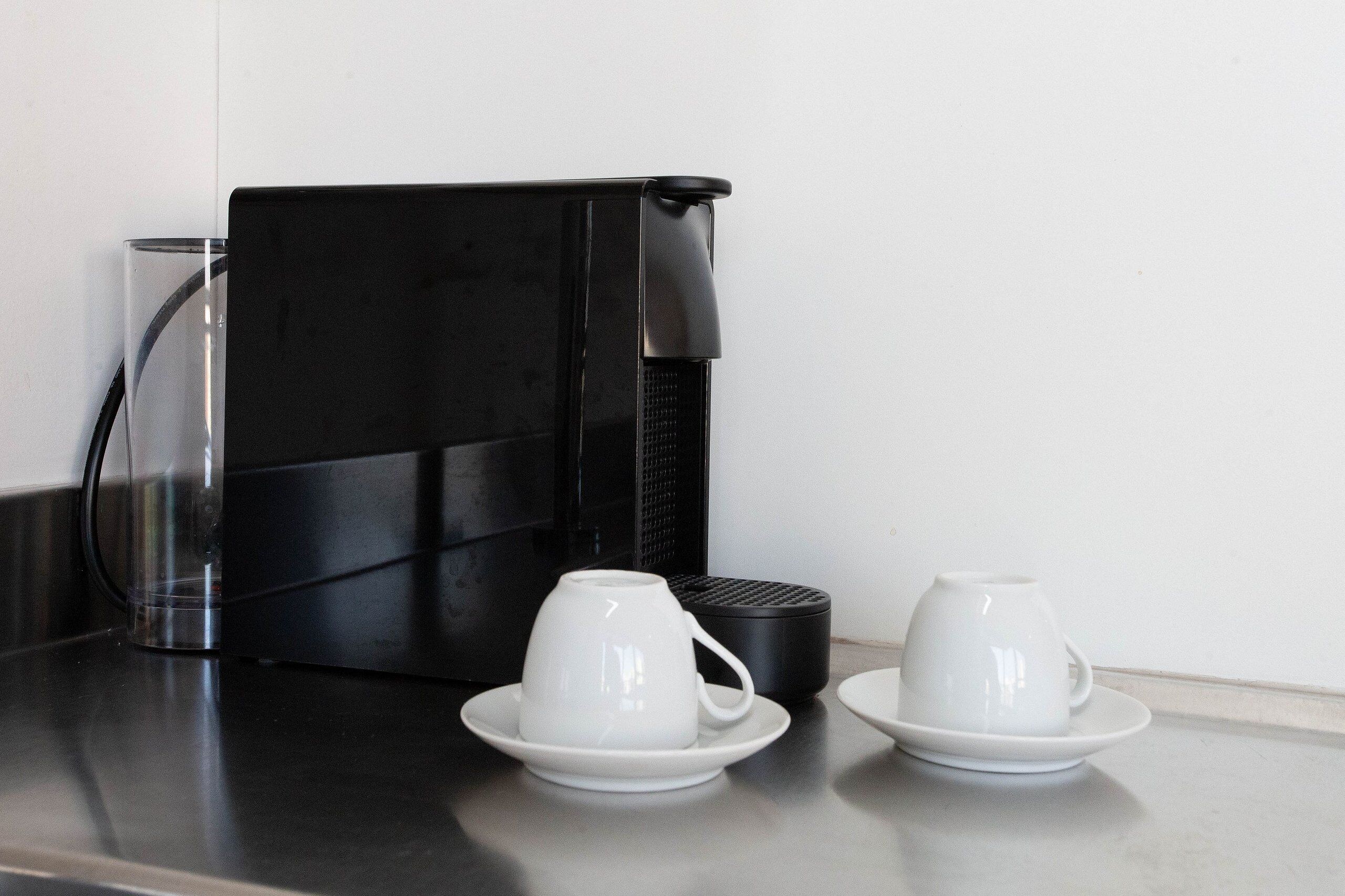 A coffee machine with two white cups on saucers on a countertop.