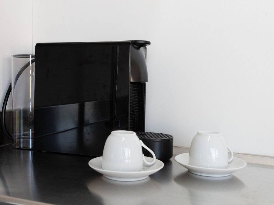 A coffee machine with two white cups on saucers on a countertop.
