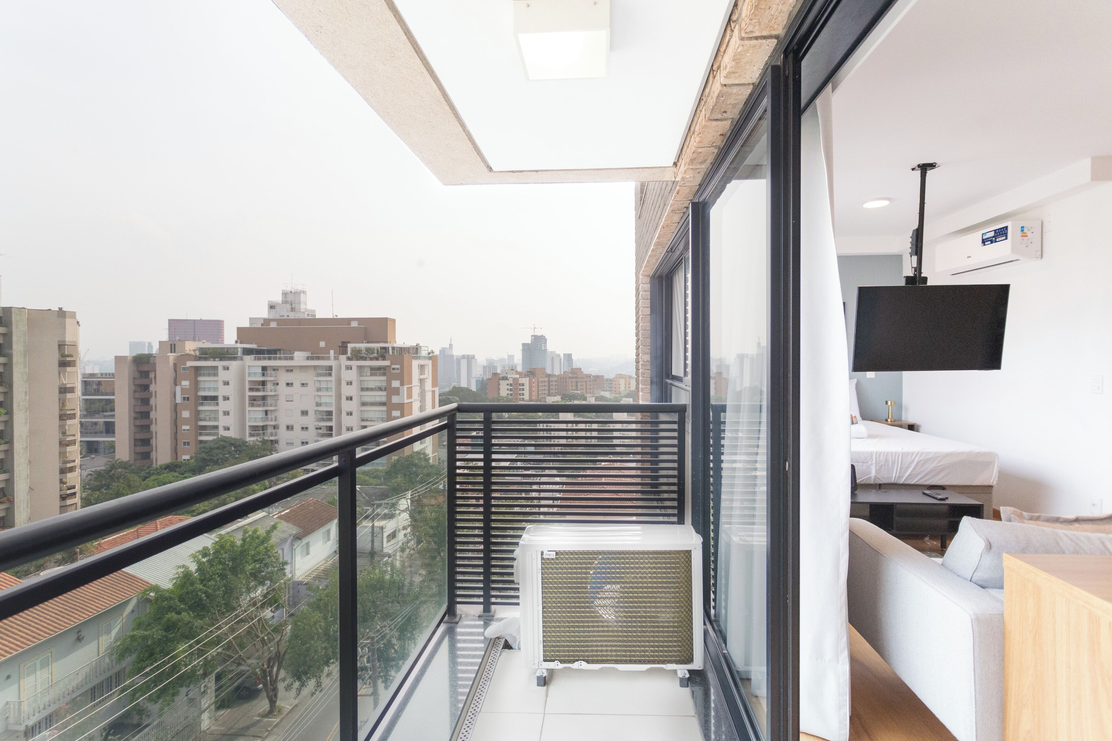 A modern apartment with a balcony, a flat-screen TV, and a view of the cityscape.