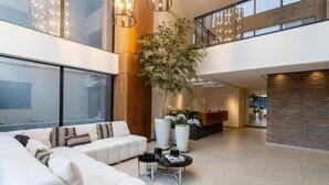 A spacious living area with a white sectional sofa, a coffee table, and large potted plants. - Condomínio Edifício Living Design (São Paulo)