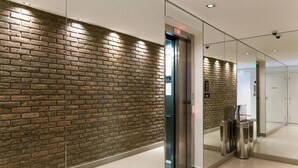 A hallway with a brick wall, an elevator, and trash bins. - Condomínio Edifício Living Design (São Paulo)