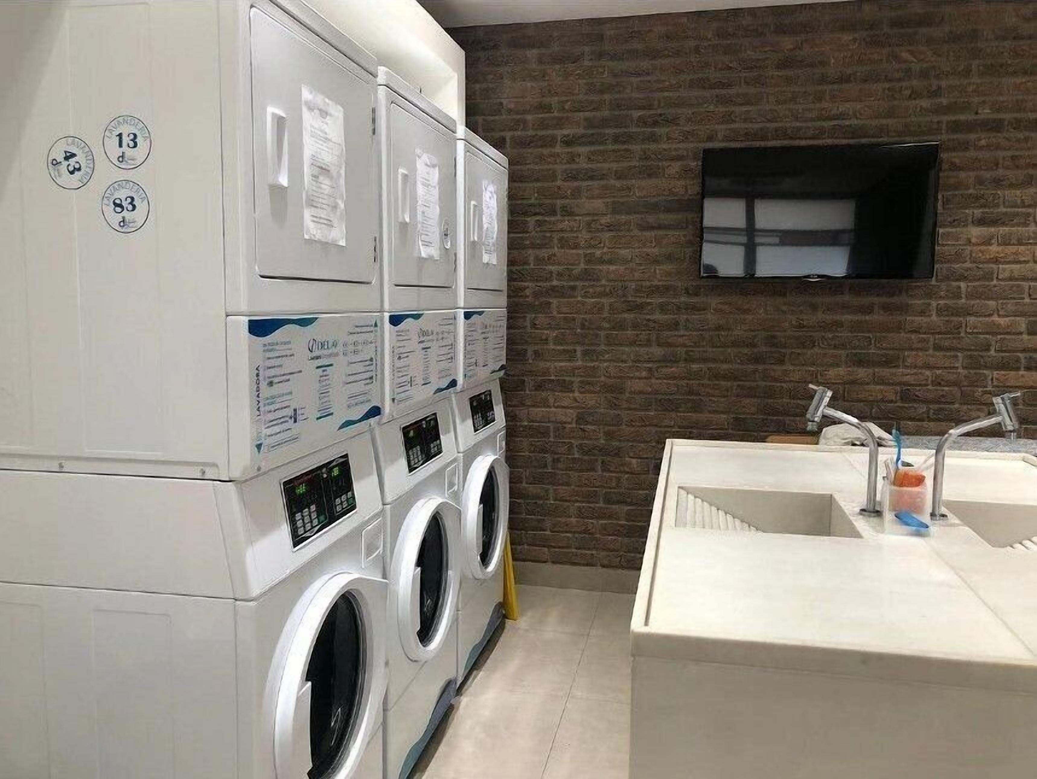 A laundry room with stacked washing machines, a brick wall, and a mounted television.