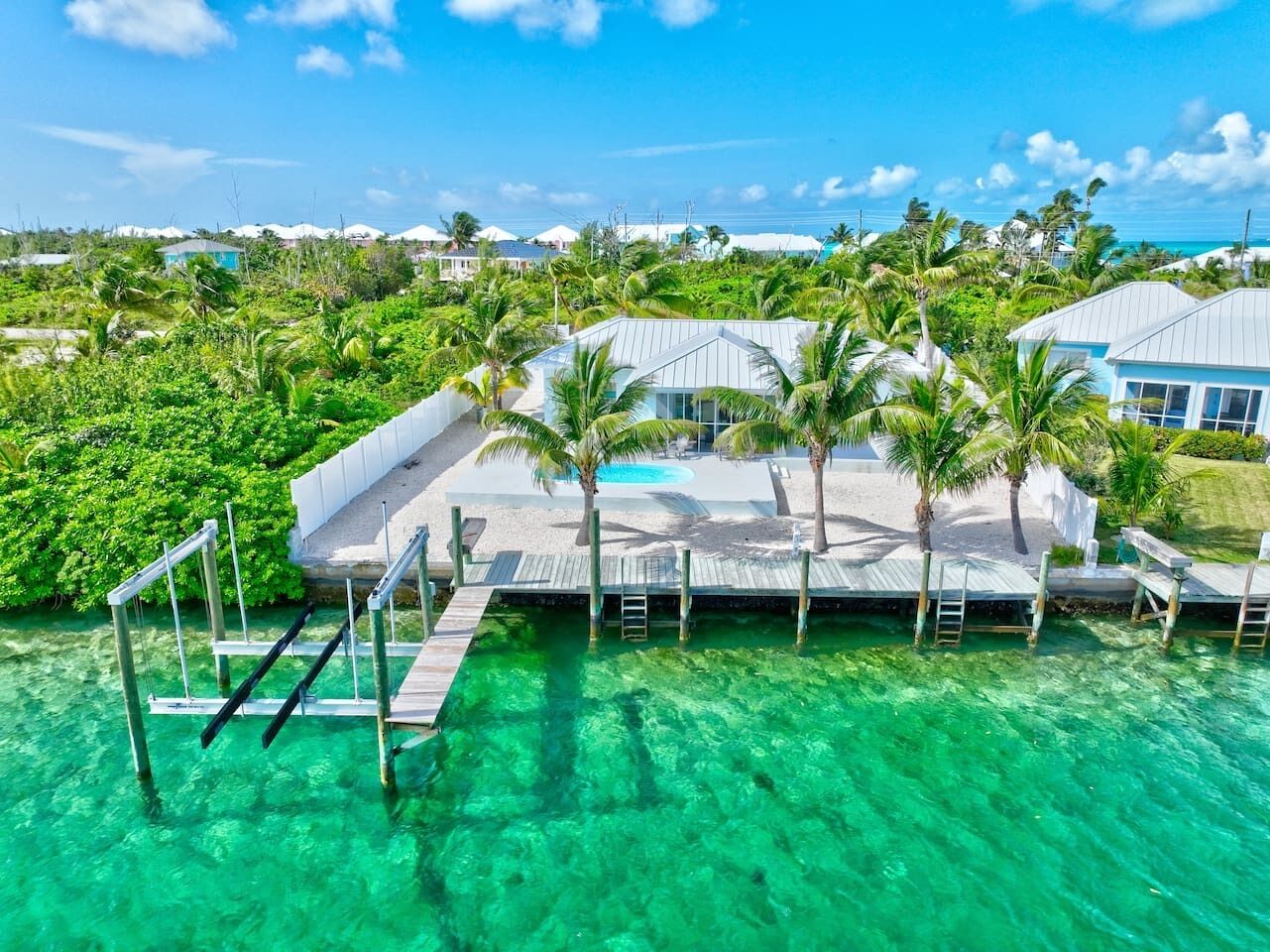 A resort with a pool area, palm trees, and clear turquoise water.