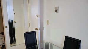 Une salle de conférence avec une table en verre, deux chaises, une porte dotée d’un miroir et un thermostat fixé au mur.
