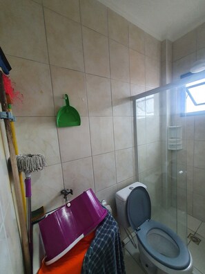 Casa de banho com sanita, chuveiro e um esfregão encostado na parede.