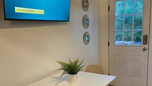 Una habitación con una televisión de pantalla plana mostrando la pantalla de activación de Roku, una mesa blanca con una planta y una tarjeta de menú, dos sillas y una puerta con ventana.