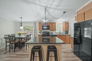 A modern kitchen with a central island, wooden cabinets, a stainless steel refrigerator, and a dining area with chairs and a table. - Pet Friendly 3BR Near Lake Norman | Extended Stays (Denver)