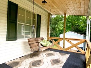 A porch with a wooden swing, a small shed in the background, and a patterned rug on the floor.