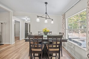 A dining area with a table and chairs, a hanging light fixture, and a window with a view of trees. - Pet Friendly 3BR Near Lake Norman | Extended Stays (Denver)