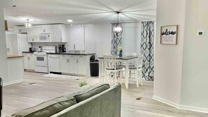 A modern living room with a grey sofa, a dining area with a white table and chairs, a kitchen with white cabinets and appliances, and a ceiling fan. - Spacious & Inviting Home in Denver, NC (Denver)