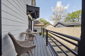 Una terraza de madera con una mesa, sillas, barandilla y vistas a casas vecinas.