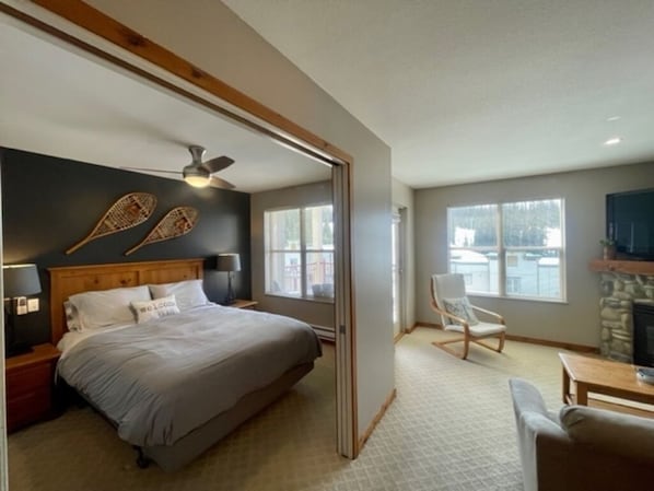 Um quarto com cama, mesas de cabeceira, ventoinha no teto e lareira.