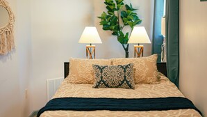 A neatly made bed with patterned bedding, two bedside lamps, a macrame wall hanging, and a large green plant. - COZY, BEAUTIFUL APARTMENT AT AVANTI COVE (Conneaut Lake)
